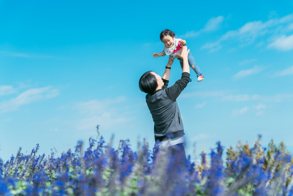 青空の下でお子さまを抱き上げるお父さん