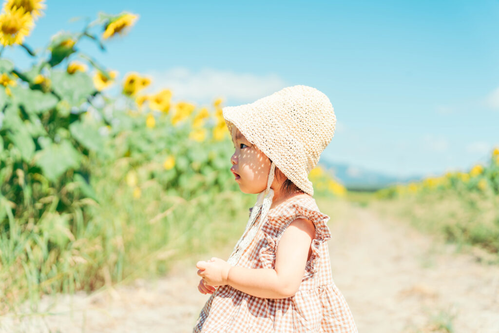 ひまわり畑で帽子をかぶった女の子